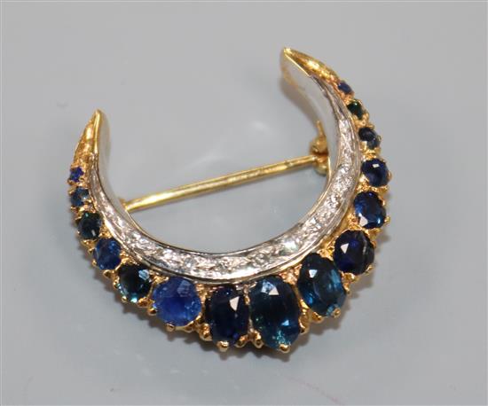 A modern yellow metal, sapphire and diamond set crescent brooch, 27mm.